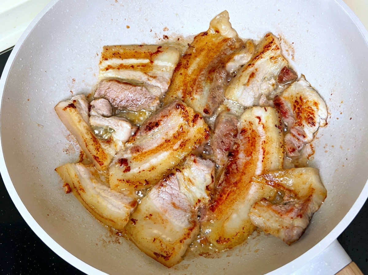 脂が溶け出し、フライパンの中でスライスされた豚バラ肉がこんがりと色づいていく様子。