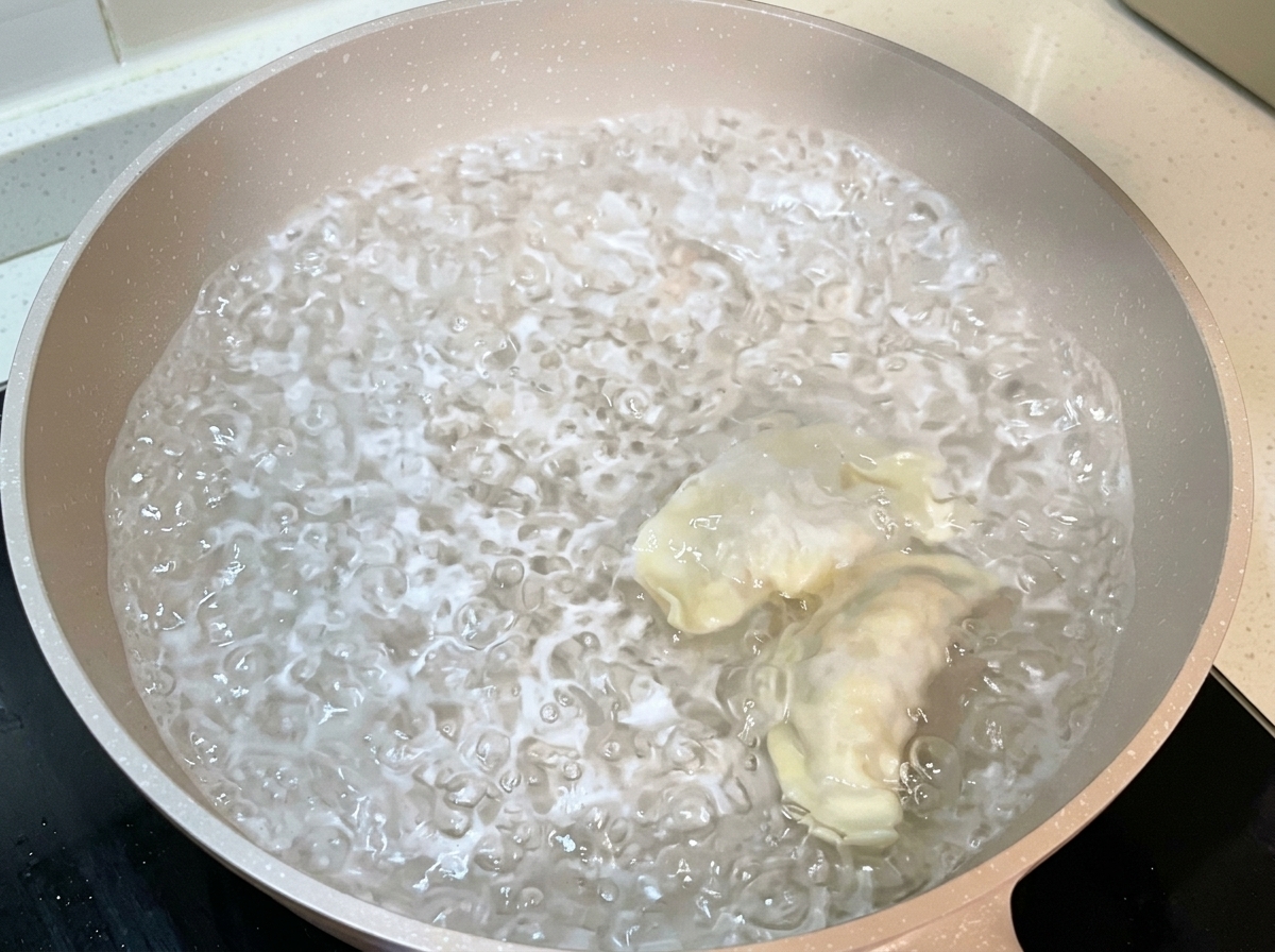 沸騰した大きなお湯の鍋に、包んだ餃子を投入している様子。
