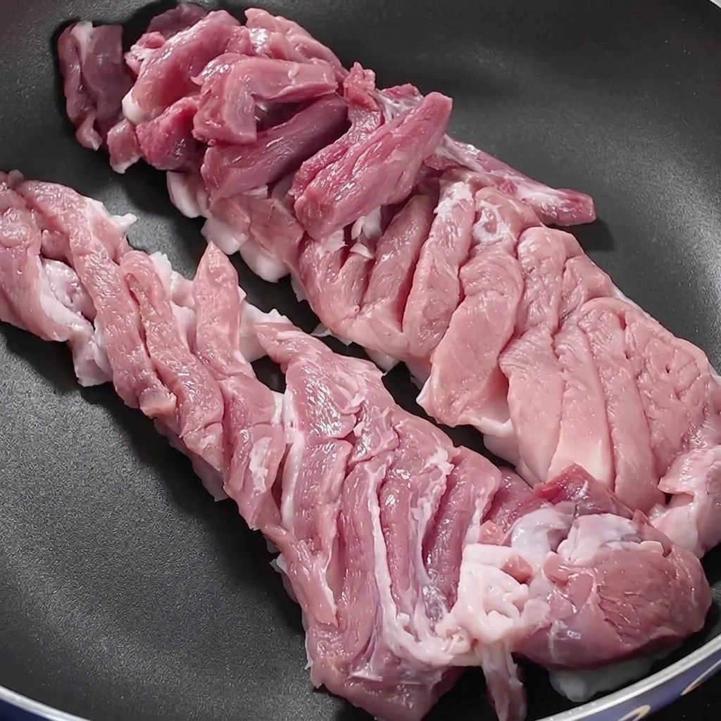 コンロの上の黒いフライパンに、スライスした豚バラ肉がきれいに並べられている様子。