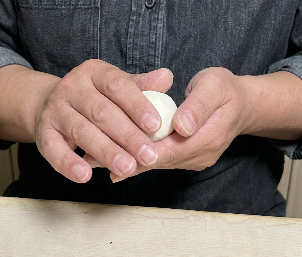 具材が入った丸い皮を、手で丁寧に包んで閉じていく様子。