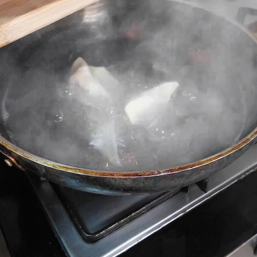 沸騰した大きなお湯の鍋の中に餃子が入っており、湯気が立ち上っている様子。