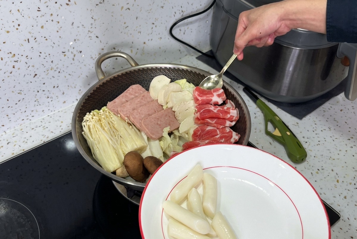 ランチョンミート、キノコ、豆腐、熟成キムチが層になり、スープを注ぐ準備ができている美しく盛り付けられた部隊チゲの鍋。