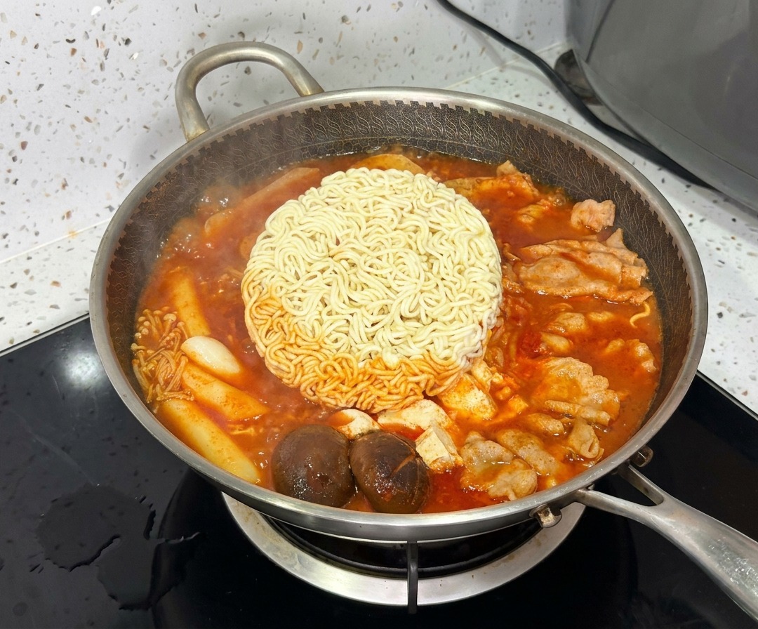 鮮やかでグツグツと煮える部隊チゲの中心で、インスタントラーメンの麺が茹で上がっている様子。