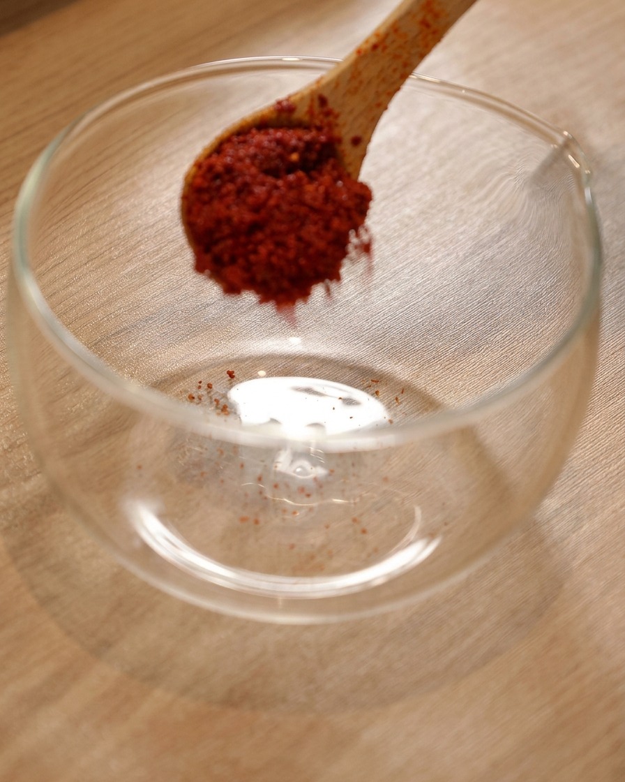 ガラスボウルに入った粉唐辛子に、韓国風ホットソースと薄口醤油が加えられている様子。