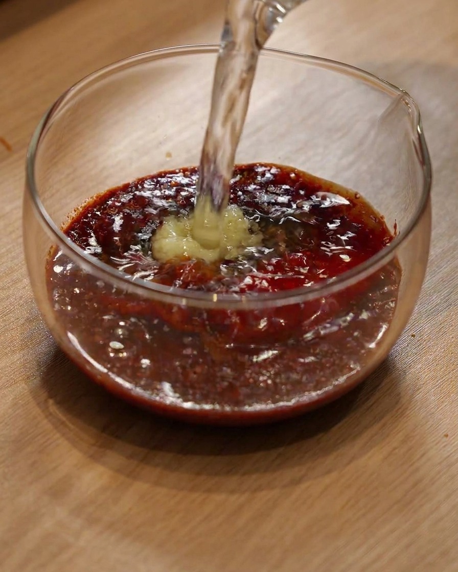 粉唐辛子と調味料が入ったガラスボウルに水が注がれている様子。