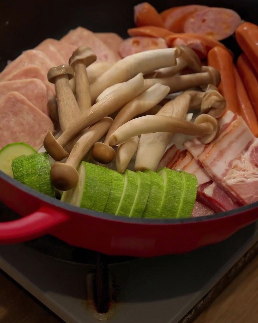 具材が並べられた鍋の中に、新鮮なえのき茸が加えられている様子。