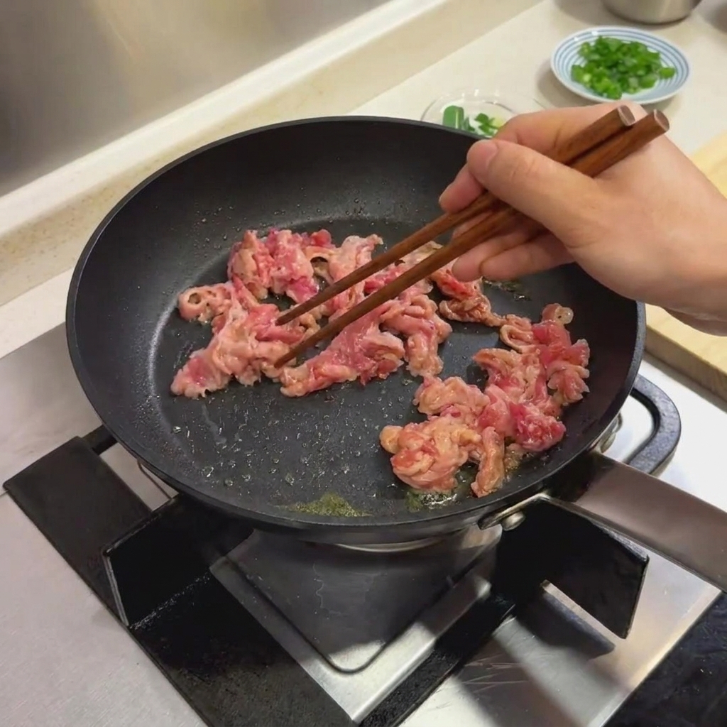 黒いフライパンでマリネした牛肉を菜箸で炒めている様子