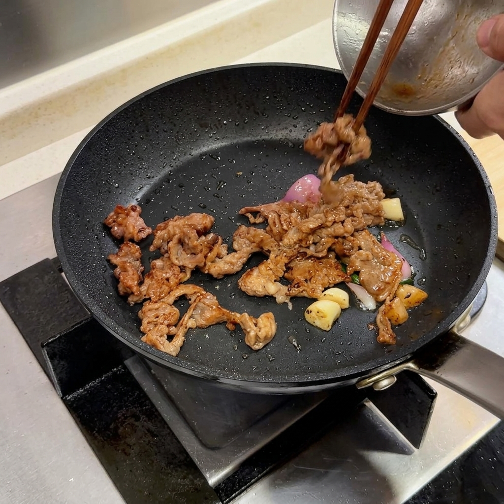 牛肉と香味野菜が入ったフライパンにバターを加えている様子