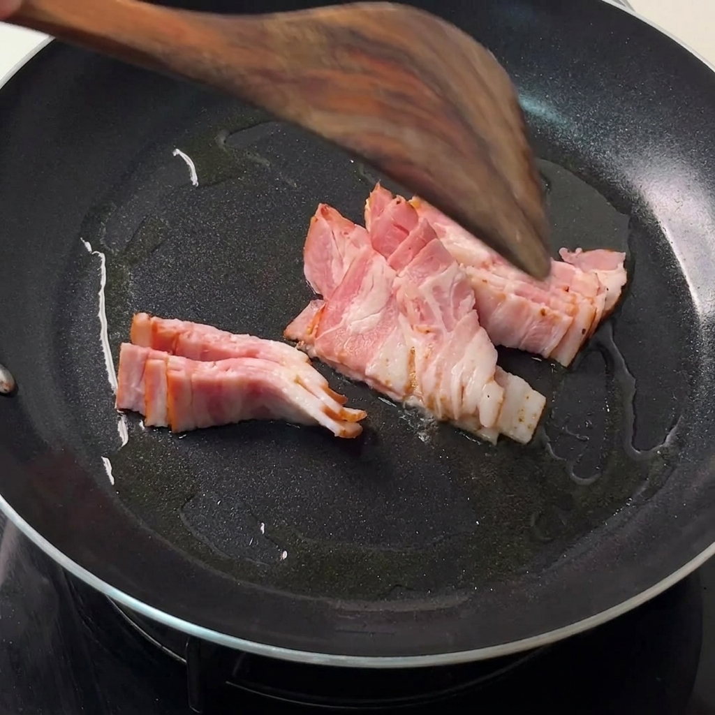 熱した黒いフライパンでベーコンがジューシーに炒められており、木製のスパチュラで裏返しているところ。