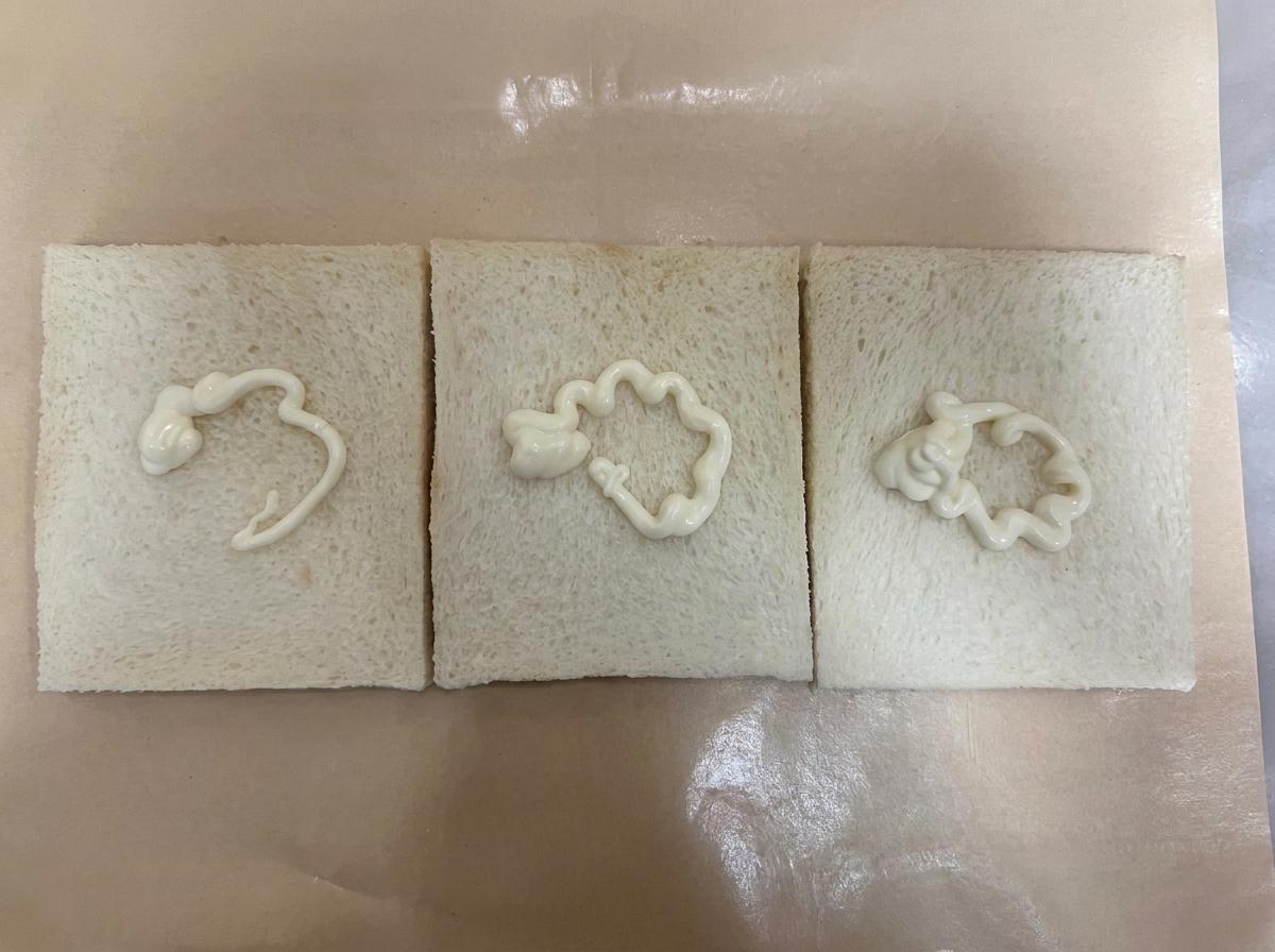 クッキングシートの上に並べられた3枚の耳なし食パン。それぞれの中央に白いドレッシングが絞られている。