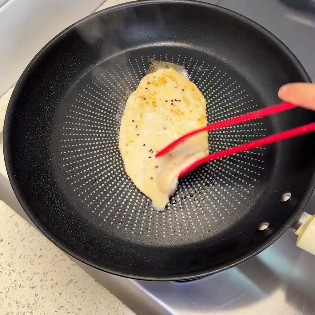 フライパンの中で、美味しそうな焼き色がついたチキンパティをトングで裏返しているところ。