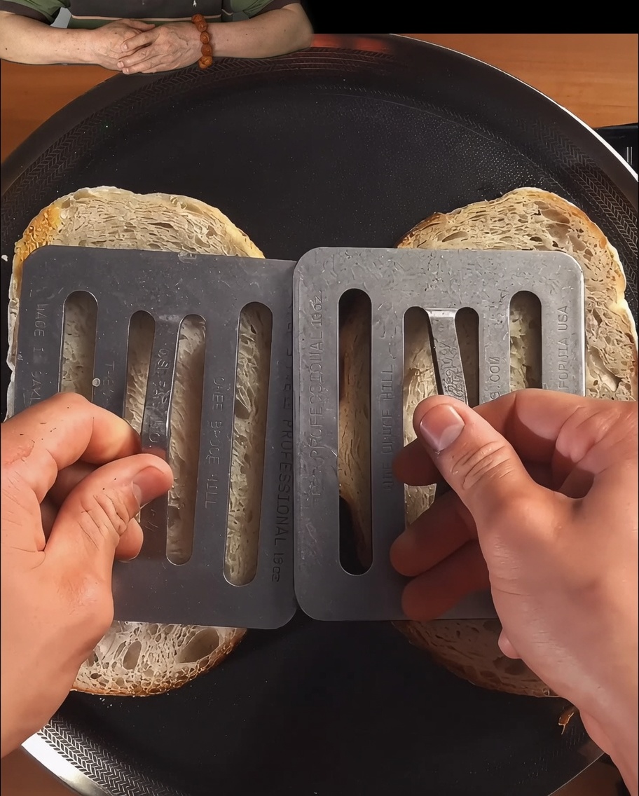 黒いスキレットの中で、プレスされながらきつね色にトーストされているパンのスライス。