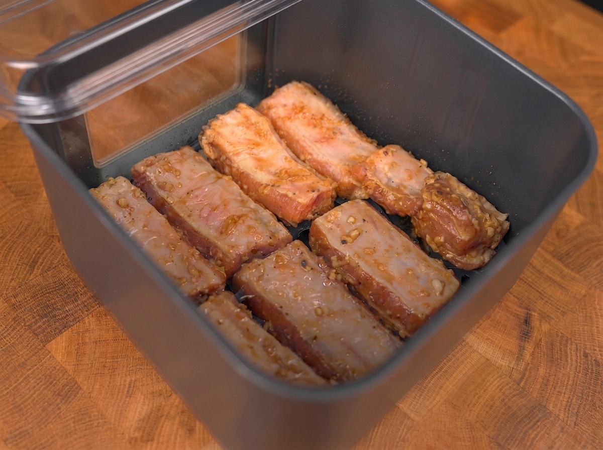 ノンフライヤーのバスケットの中に重ならないように並べられた、下味のついたポークリブ。