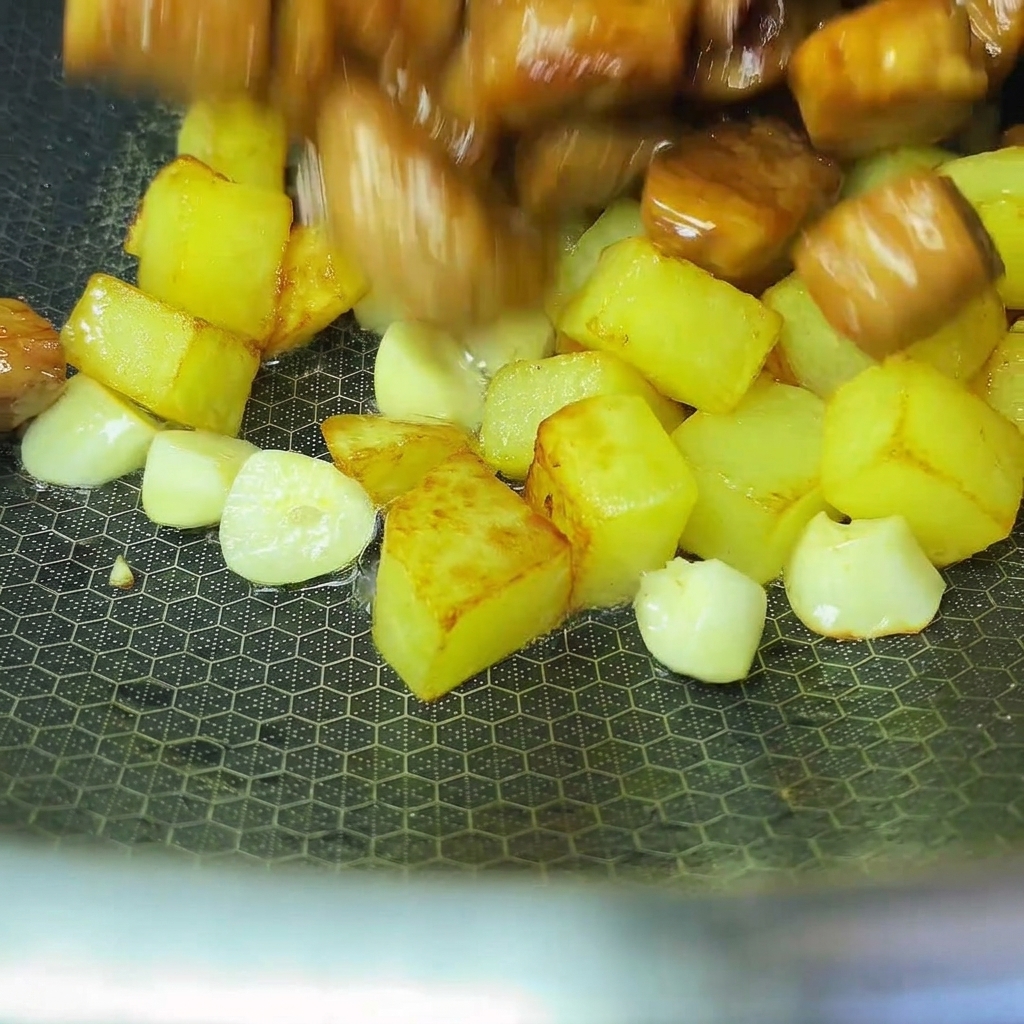 炒めたじゃがいもと豚肉を中華鍋で合わせている様子。