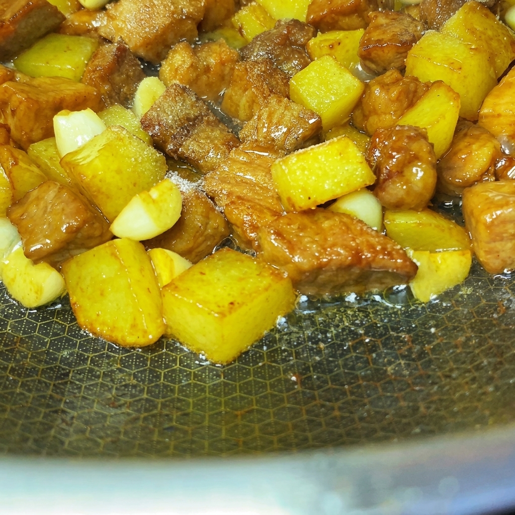 炒めた豚肉とじゃがいもの上にスパイスとごまが均等に振りかけられている様子。
