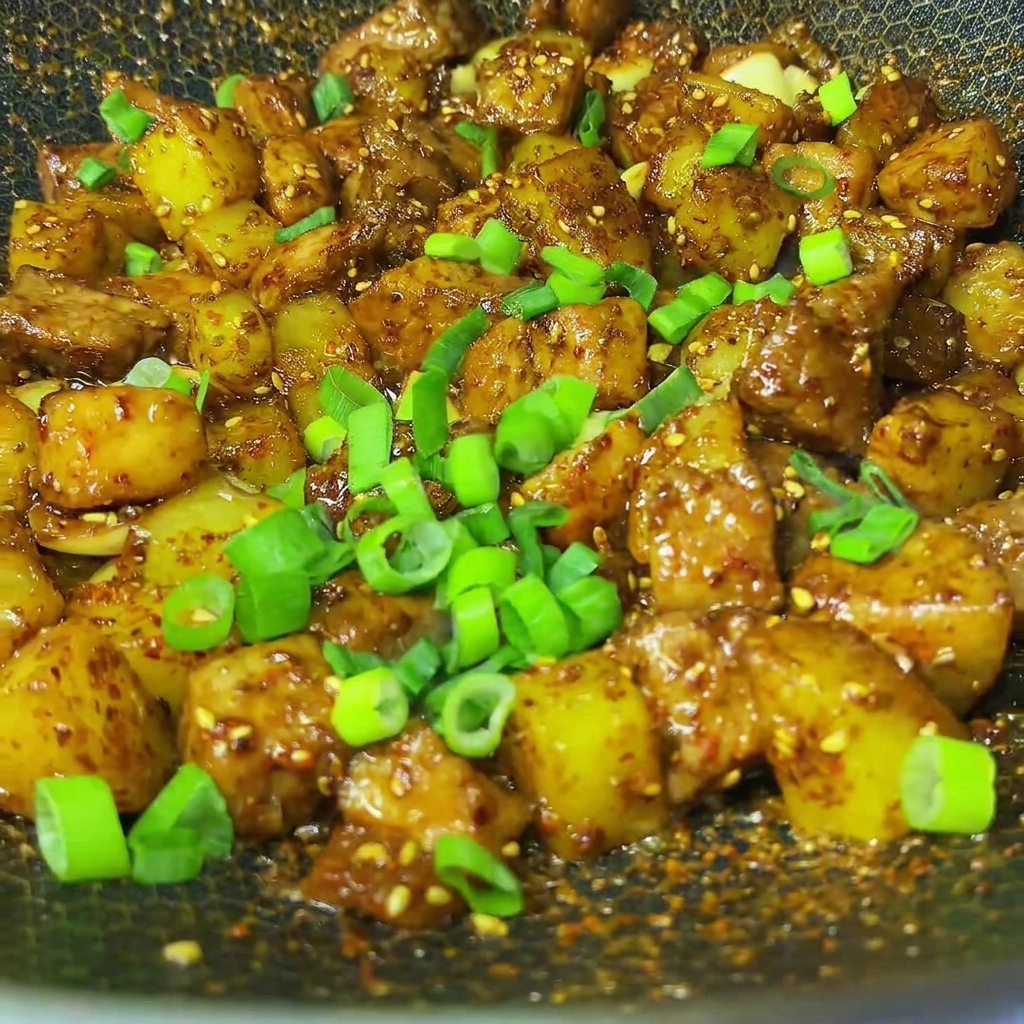 完成した豚肉とポテトのクミン炒めの上に、刻みたての青ねぎが振りかけられている様子。