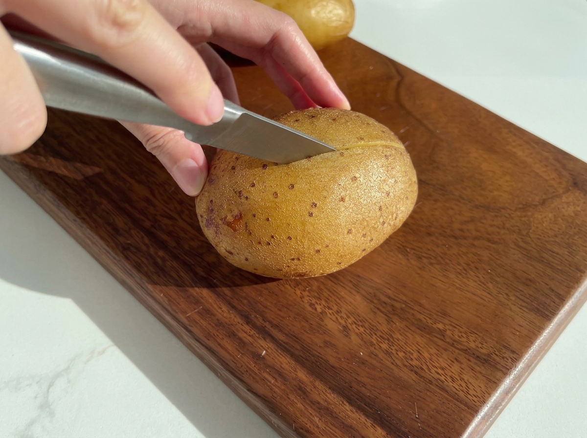 木製のまな板の上で、ナイフがベイクドポテトを縦半分に切り分けているところ。