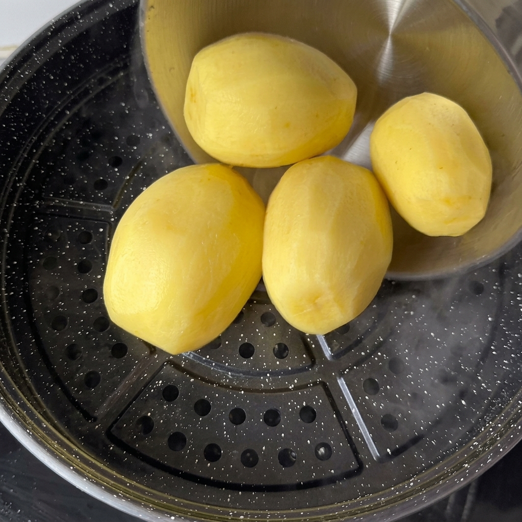 沸騰したお湯の上にセットした蒸し器に、皮をむいたじゃがいもを並べる様子。