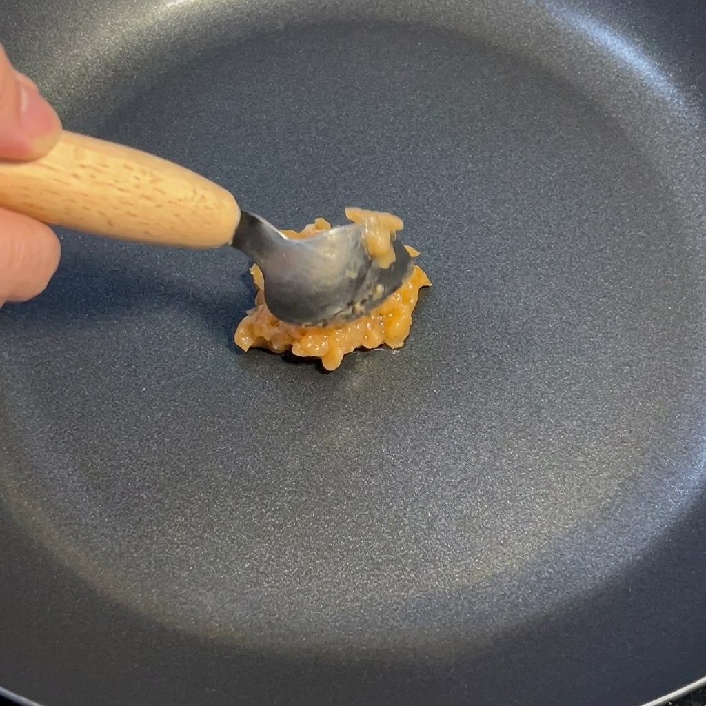 黒いフライパンの中で、スプーンを使ってにんにく生姜ソースを弱火で炒めている様子。