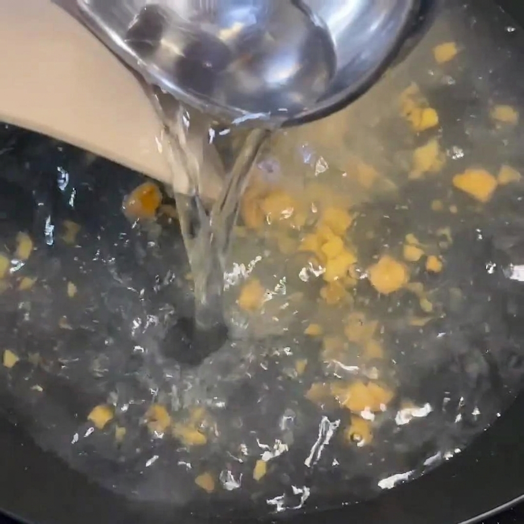 お玉から、調味料と生姜の入った沸騰した鍋にお湯を注いでいる様子。