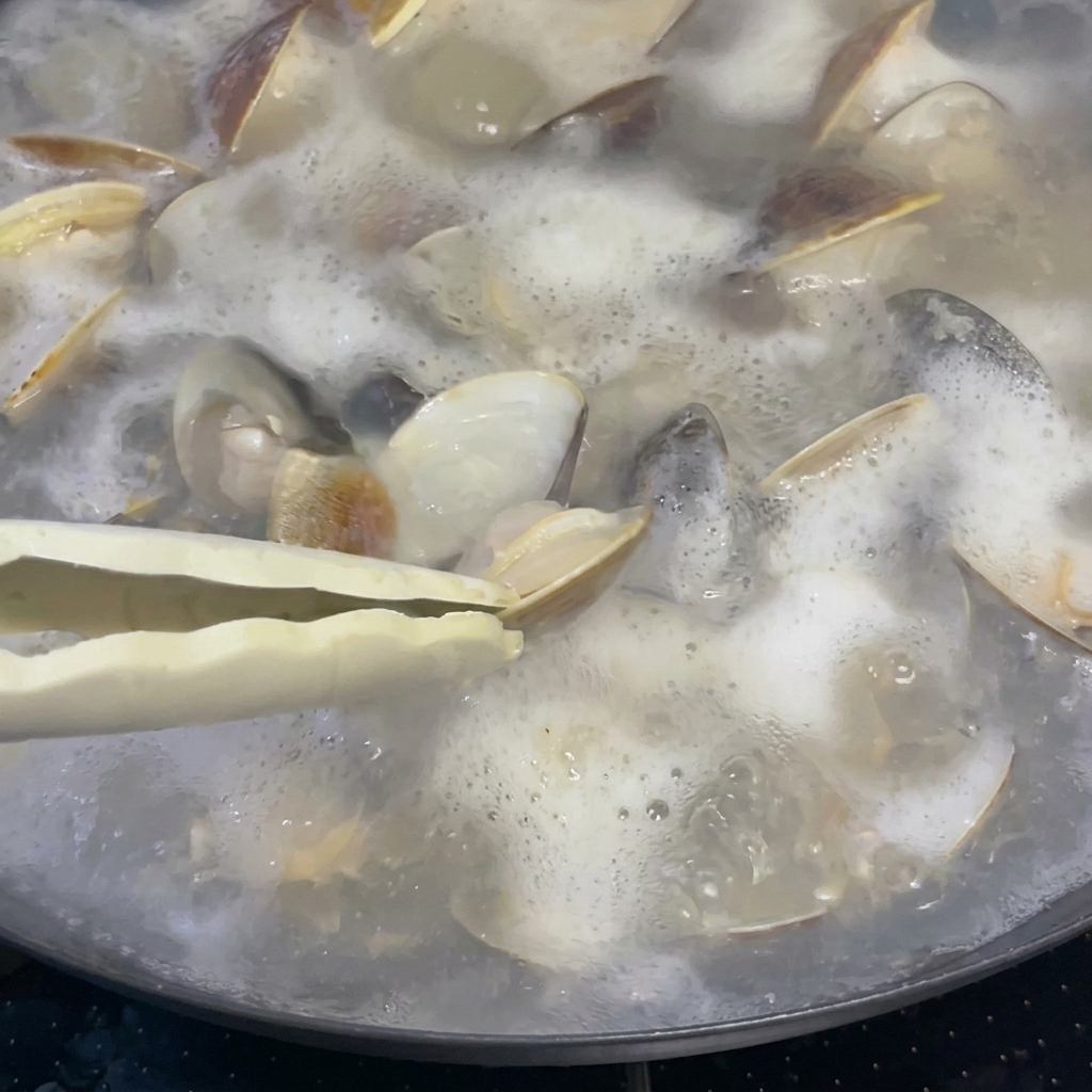 あさりとスープが煮立っている鍋に、大さじ1杯の料理酒を注いでいる様子。