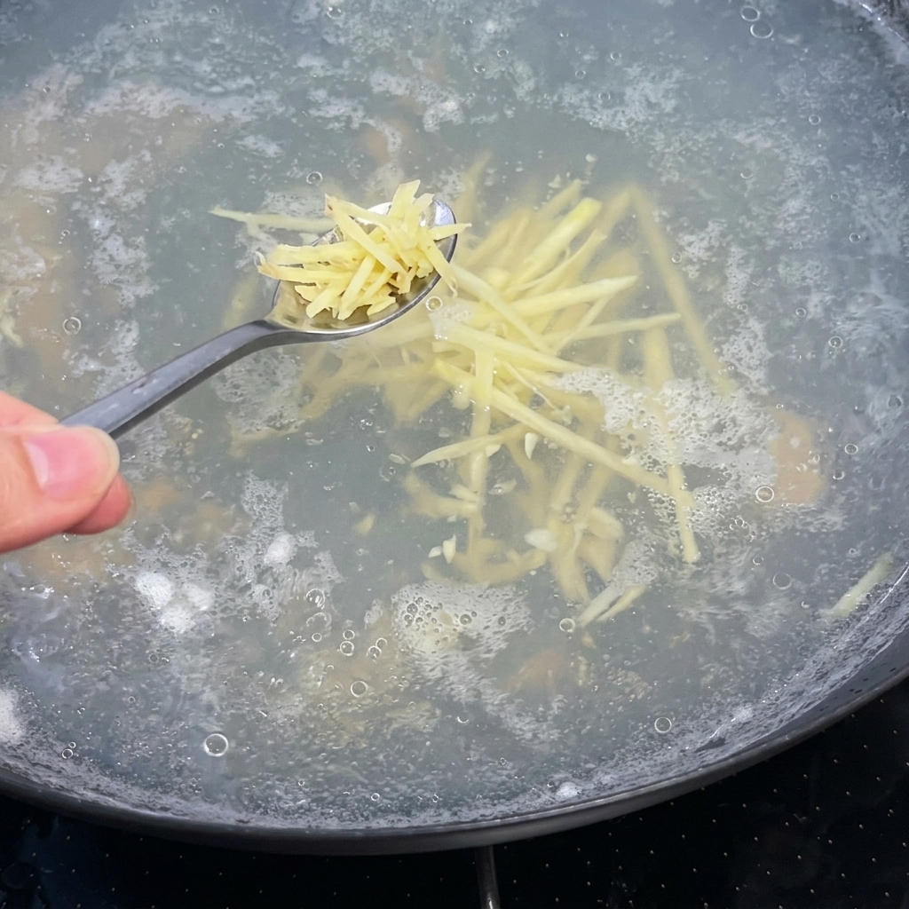 沸騰した透明なスープの鍋に、スプーン一杯の千切り生姜を加えている様子。