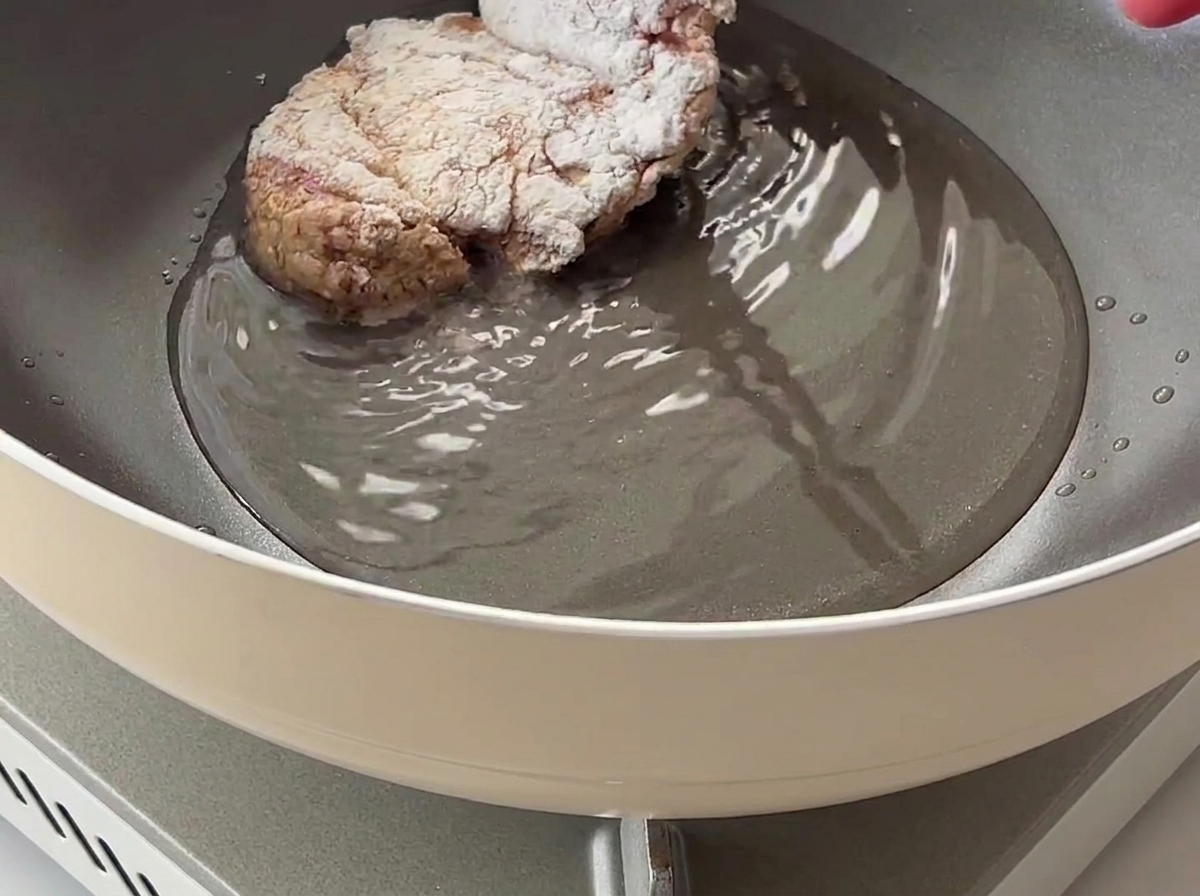 粉をまぶした鶏肉を、熱い油の入ったフライパンに入れている様子。