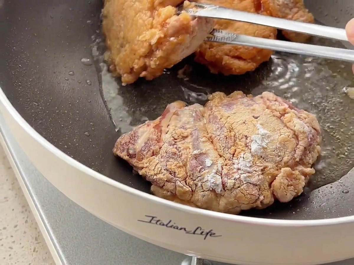 フライパンの中でトングを使って鶏肉を裏返し、こんがりとカリカリに焼けた表面を見せている様子。