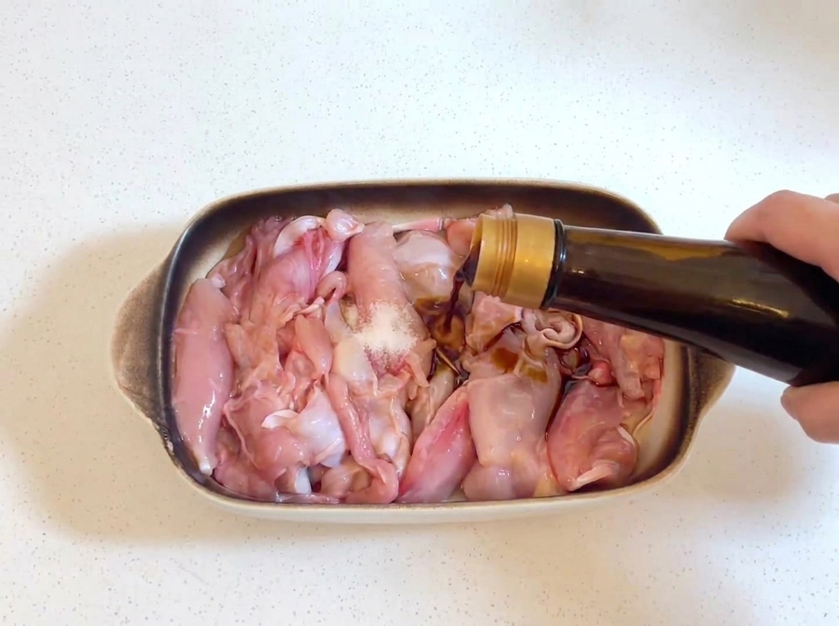 ガラス瓶から生の鶏肉に醤油が注がれている様子。鶏肉には少量の塩が見える。
