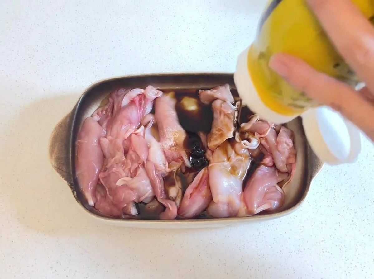 醤油ベースのマリネ液に浸かった生の鶏肉に、黄色いボトルからドロッとした濃い色のオイスターソースが絞り出されている様子。