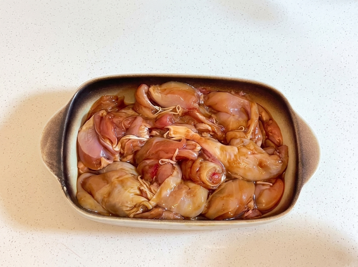 マリネした鶏肉が入った長方形の陶器の耐熱皿に、透明なラップがしっかりと掛けられている様子。