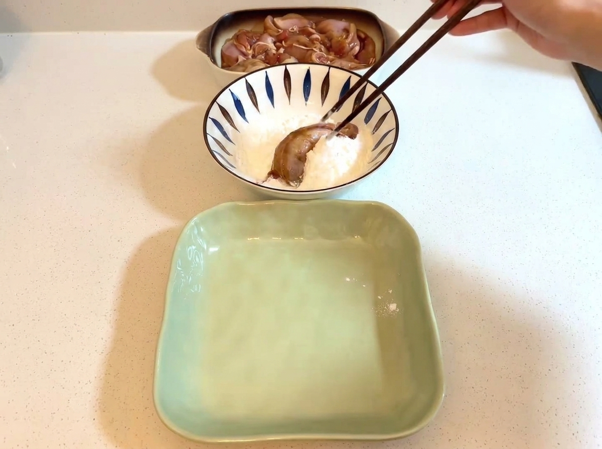 白い片栗粉が入ったボウルの中で、マリネした鶏肉を箸でつまんでいる様子。