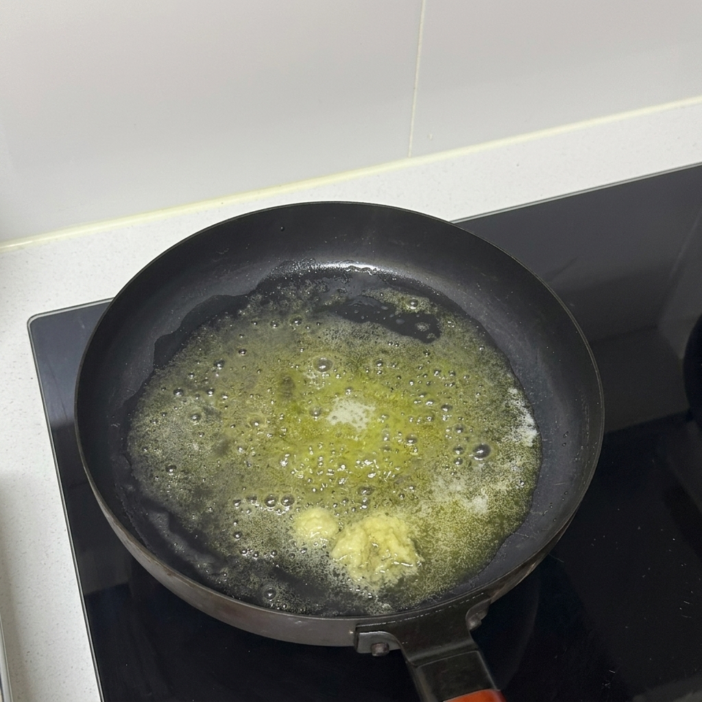 フライパンの溶かしバターの中でみじん切りにしたにんにくを炒めている様子。