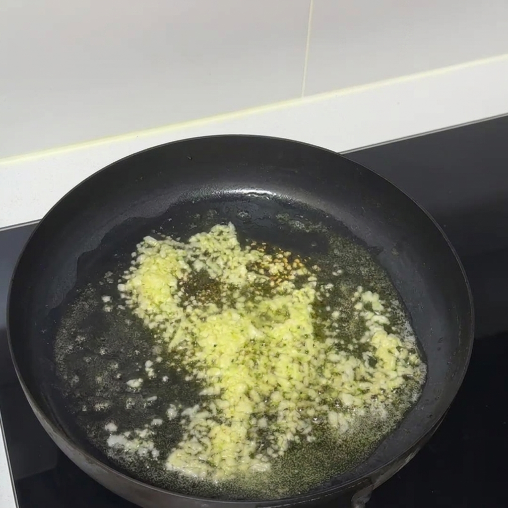 黒いテフロン加工のフライパンの中で、みじん切りのにんにくと溶けたバターがジュージューと音を立てている様子。