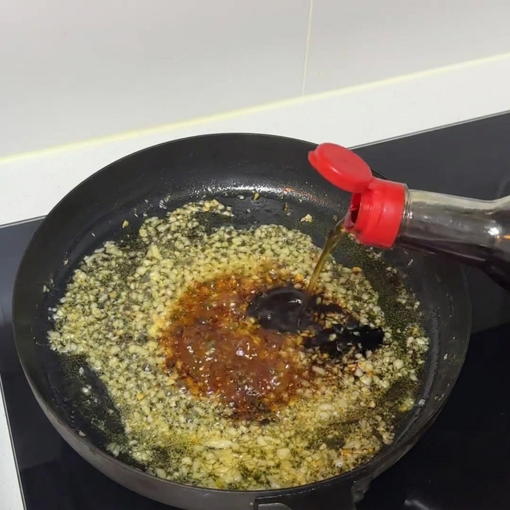 フライパンの中でみじん切りにんにくと一緒に、濃い色のソースが煮立たせながらかき混ぜられている様子。