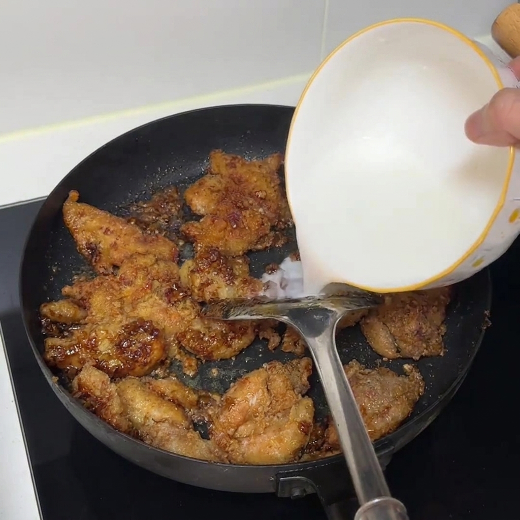 火を通した鶏肉が入ったフライパンに、白いボウルから水溶き片栗粉が注がれている様子。