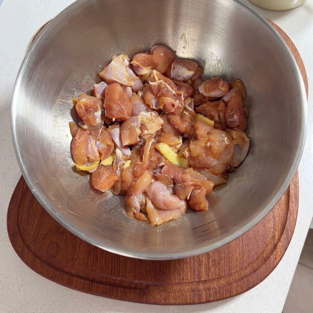 一口大に切った生肉の鶏もも肉に、タレと生姜の薄切りが入った金属製のボウル。