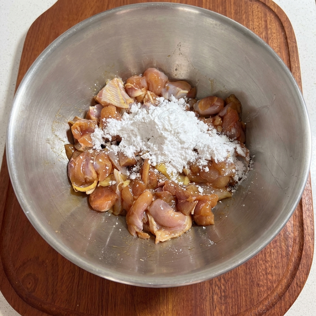 下味をつけた鶏肉に、金属製のボウルの中で白い片栗粉を手で混ぜ合わせている様子。