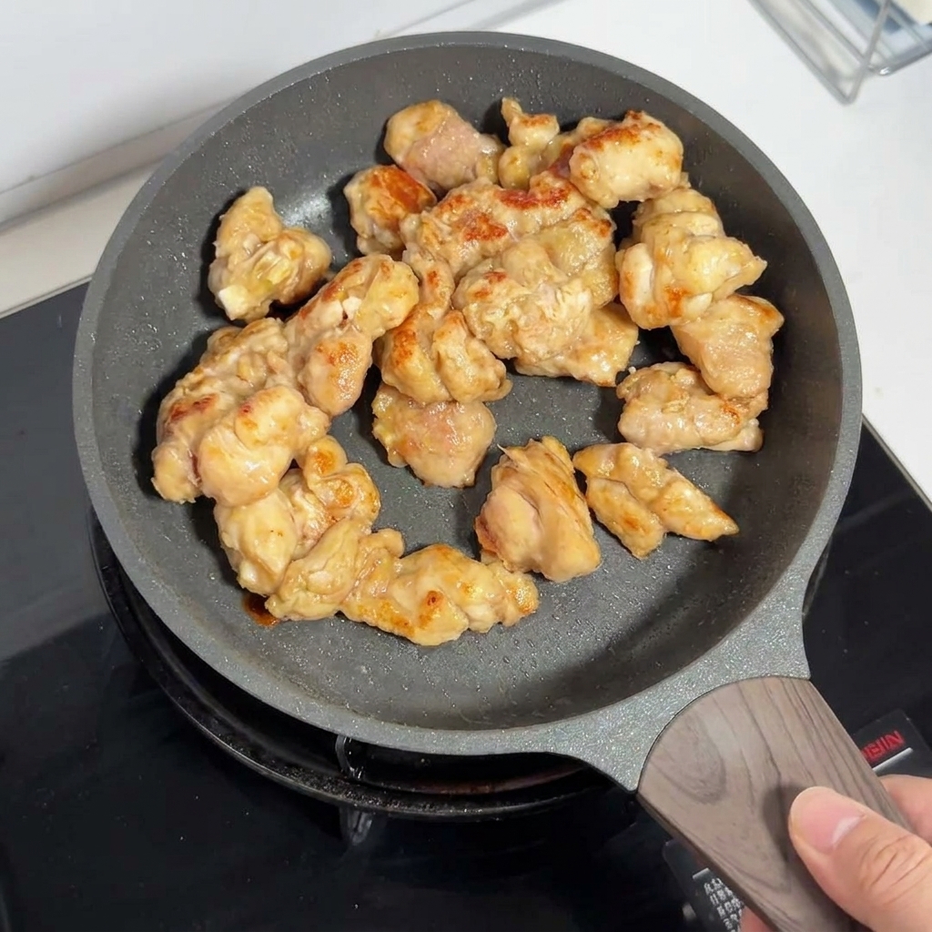ノンスティックフライパンの中でこんがりときつね色に揚げ焼きにされている鶏もも肉。