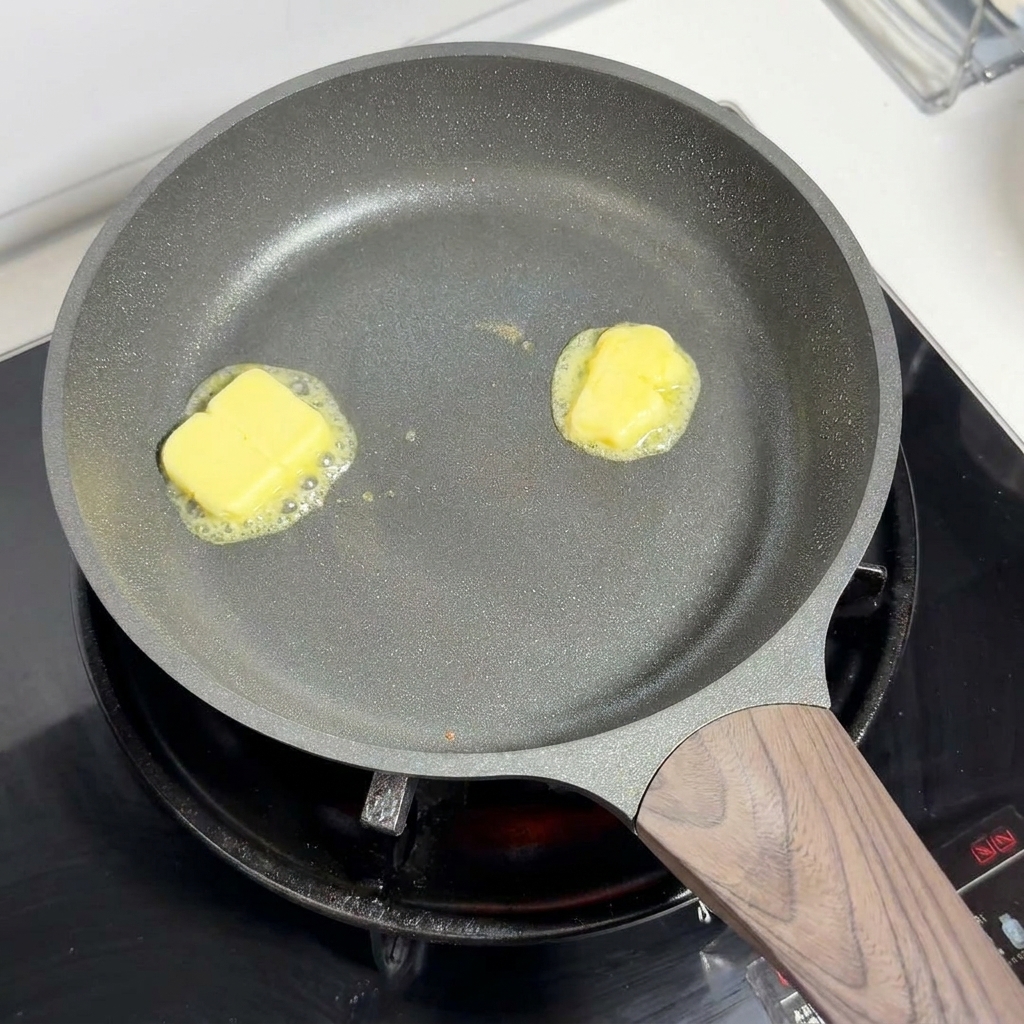 弱火のフライパンの中で、黄色いバターの塊が溶けて泡立っている様子。