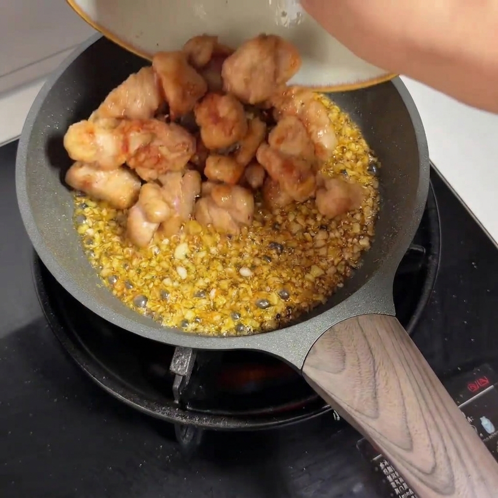 ガーリックソースの入ったフライパンに、皿に盛られた下焼き済みの鶏肉を投入しているところ。