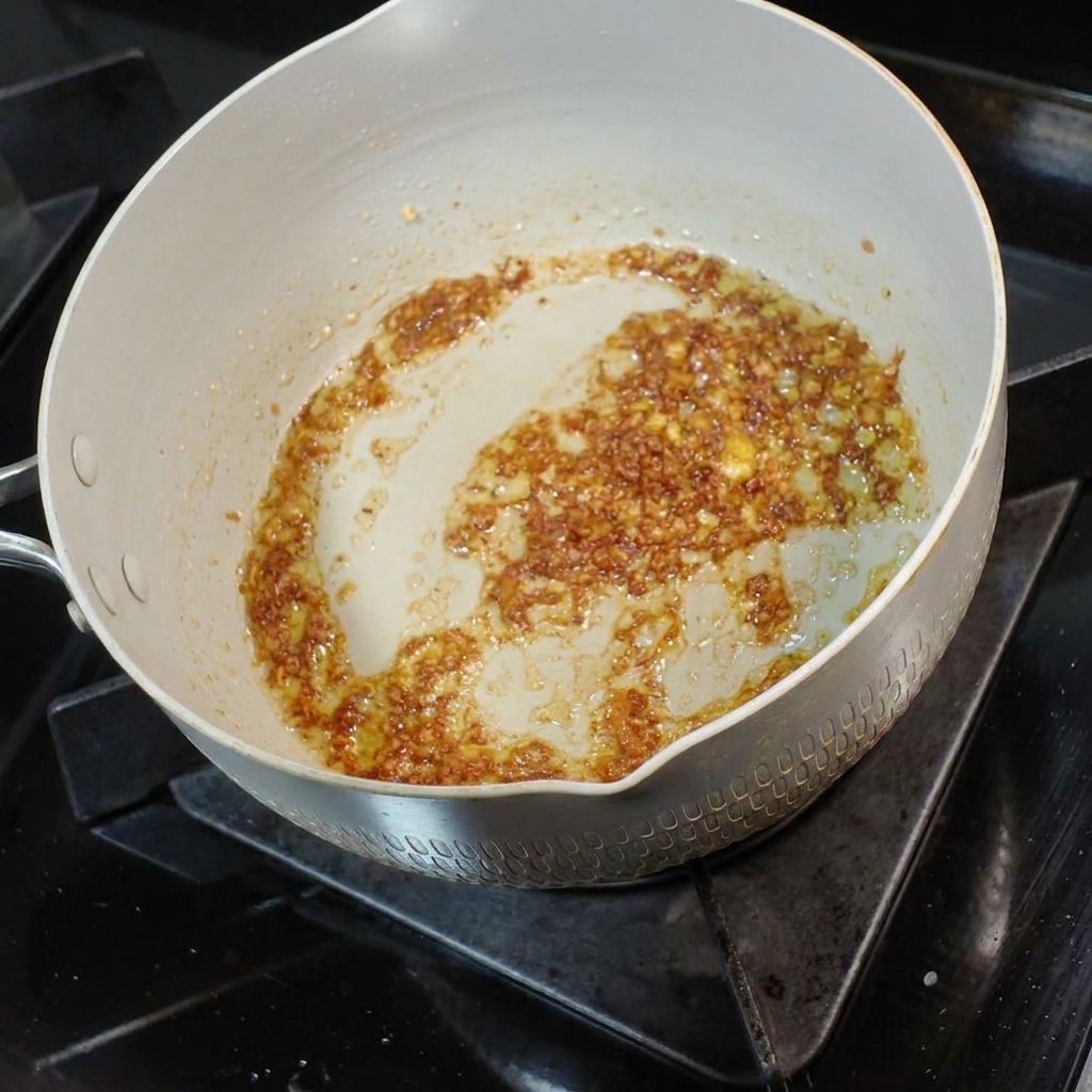 風味豊かなニンニクバターの混合物に、小さなお玉一杯の麺スープが注がれている様子。