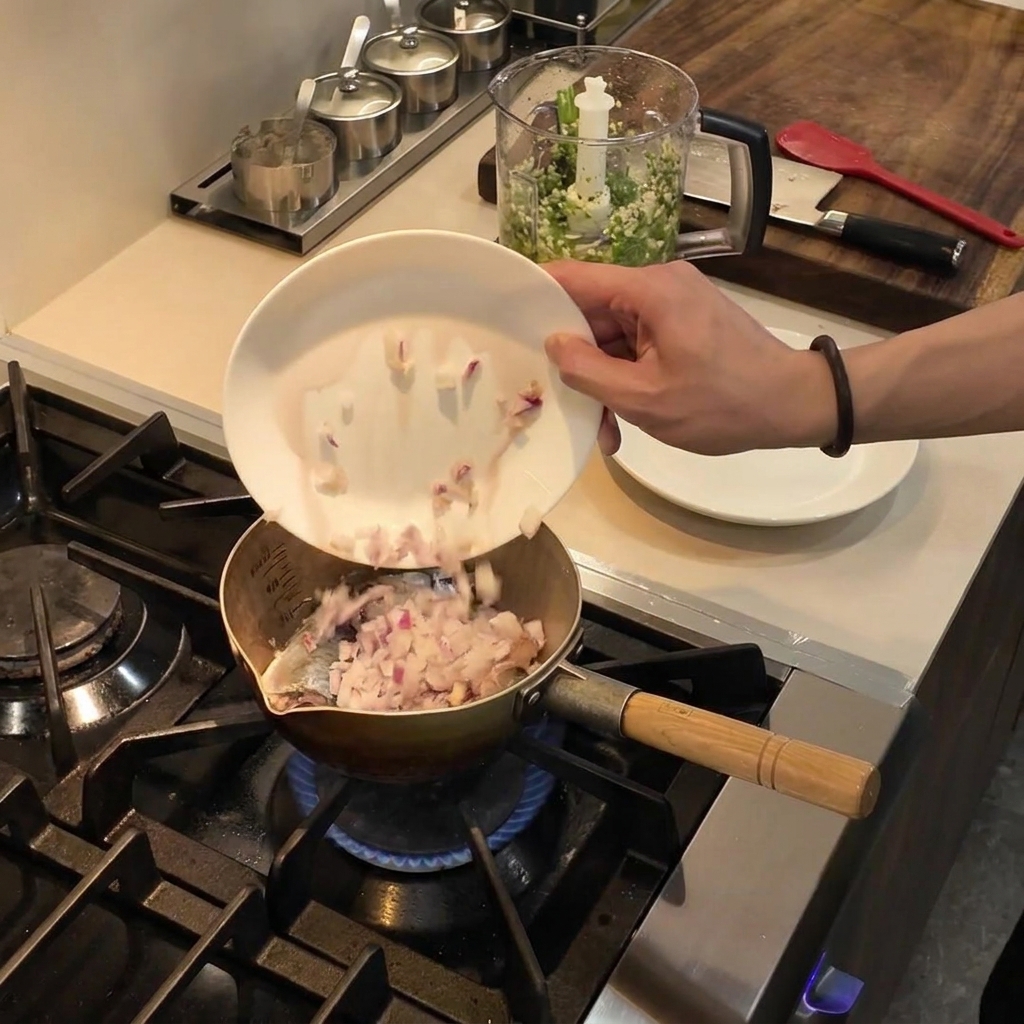 白い皿から、コンロの上の熱した油が入った鍋へとダイス状の赤玉ねぎが滑り落ちている様子。