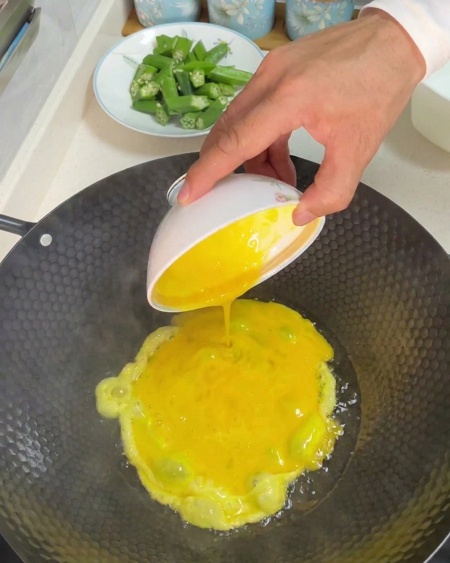 油を熱した中華鍋に溶き卵を注ぎ入れる様子。