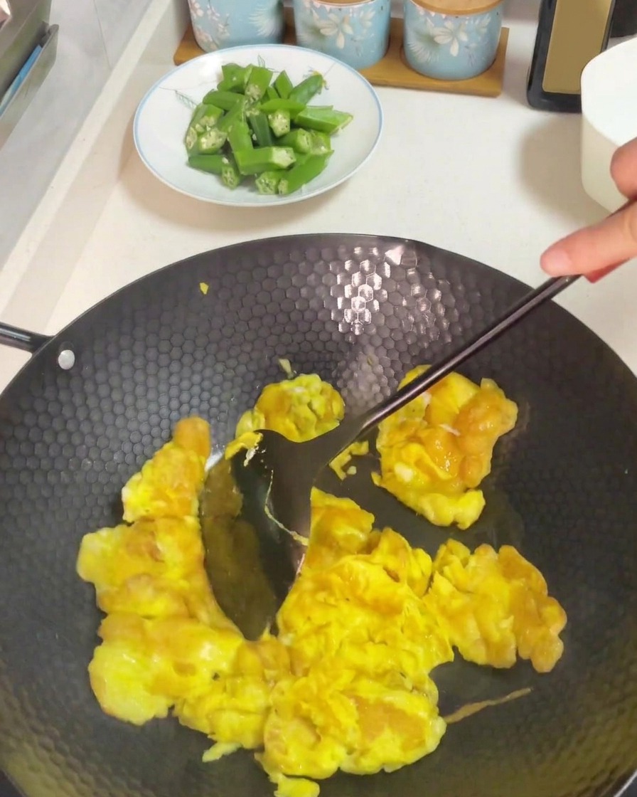 ヘラを使って中華鍋で卵をかき混ぜながら炒める様子。