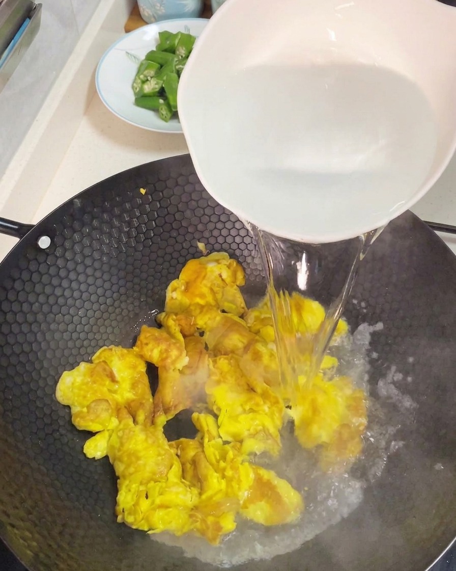 炒めた卵の上から熱湯を注ぎ、スープのベースを作る様子。