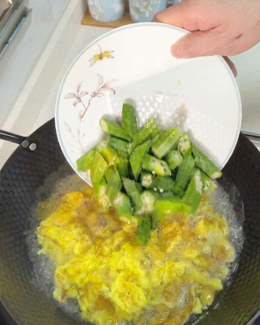 ぐつぐつと煮立つ卵スープに、斜め切りにしたオクラを加える様子。