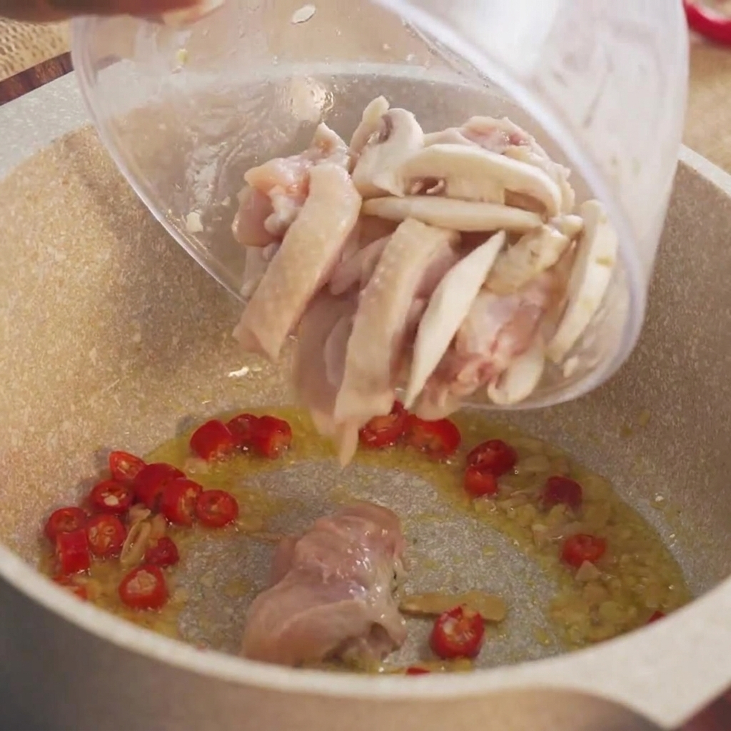 ボウルから下味をつけた生の鶏肉の塊を熱い鍋に流し込んでいる様子。
