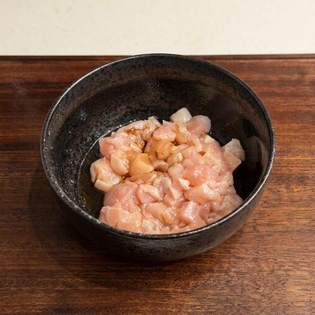 黒いボウルに入れられた生の角切り鶏肉に、醤油が注がれているところ。