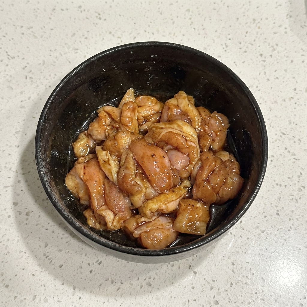 黒いボウルの中で、下味の調味料と生の鶏肉片がしっかりと混ぜ合わされている様子。